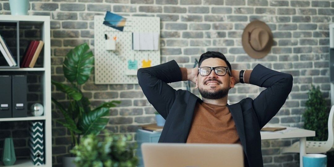 selected-01-office-desk-stretch-optimized Man lutar sig bakåt vid skrivbordet och tar en paus från skärmarbete